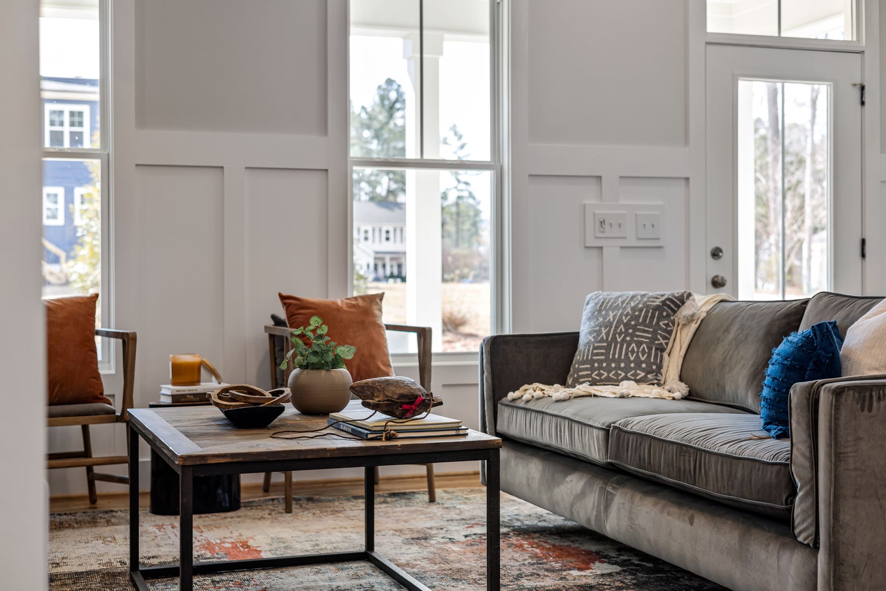 A bright living room with a gray sofa, tall windows, and natural light